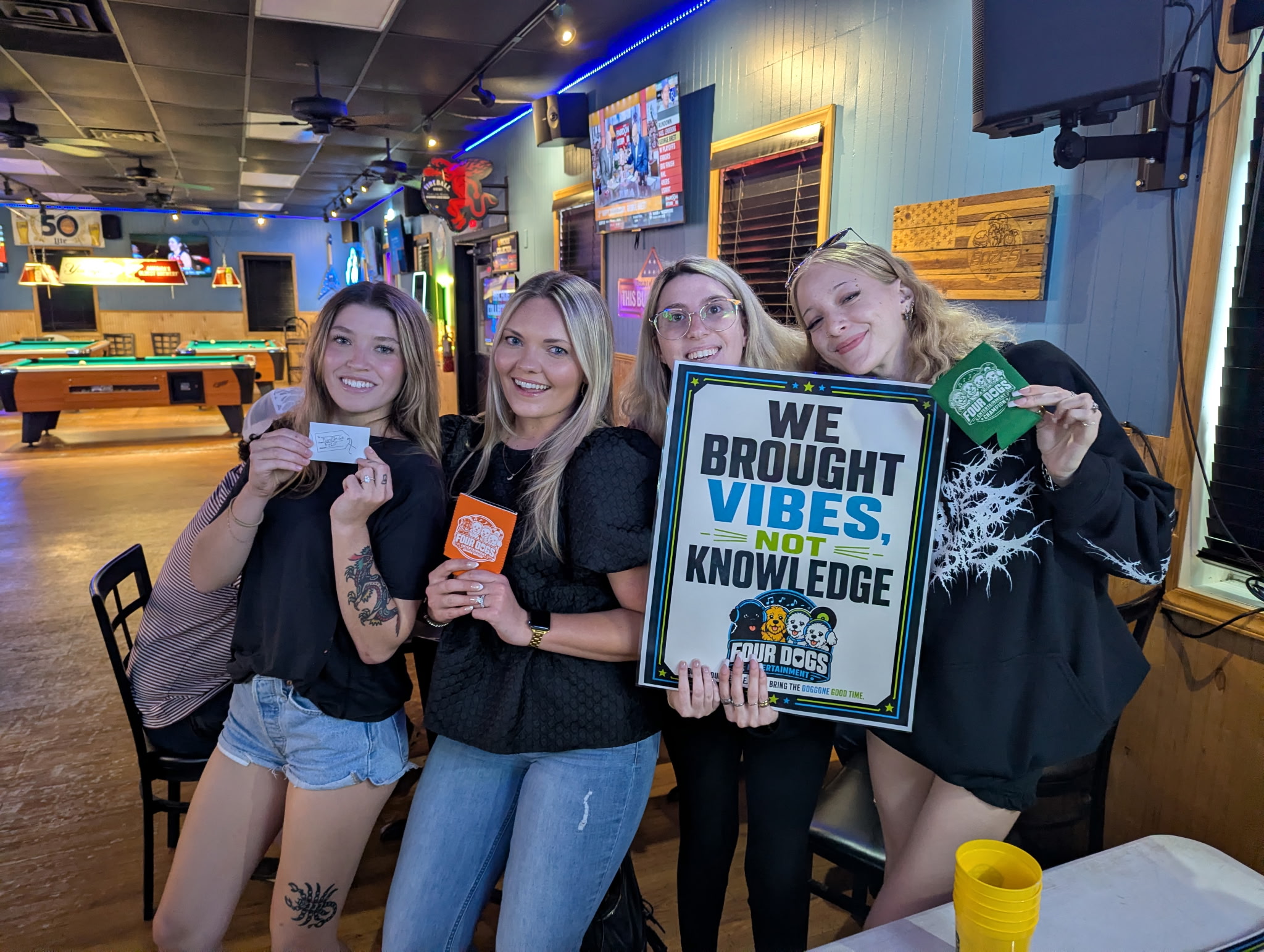Four women at Four Dogs Entertainment Survey Showdown at Boze’s Restaurant & Bar holding a Four Dogs sign and branded koozies