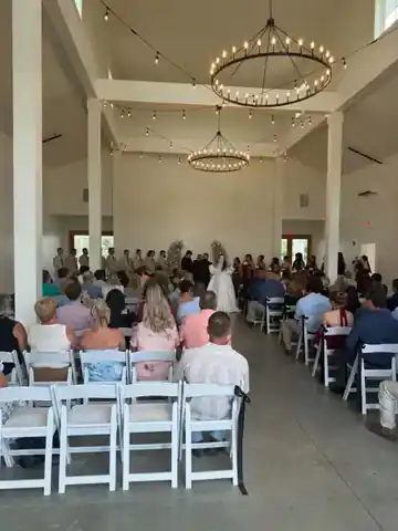 Wedding ceremony inside a bright reception venue with guests seated on both sides of the aisle